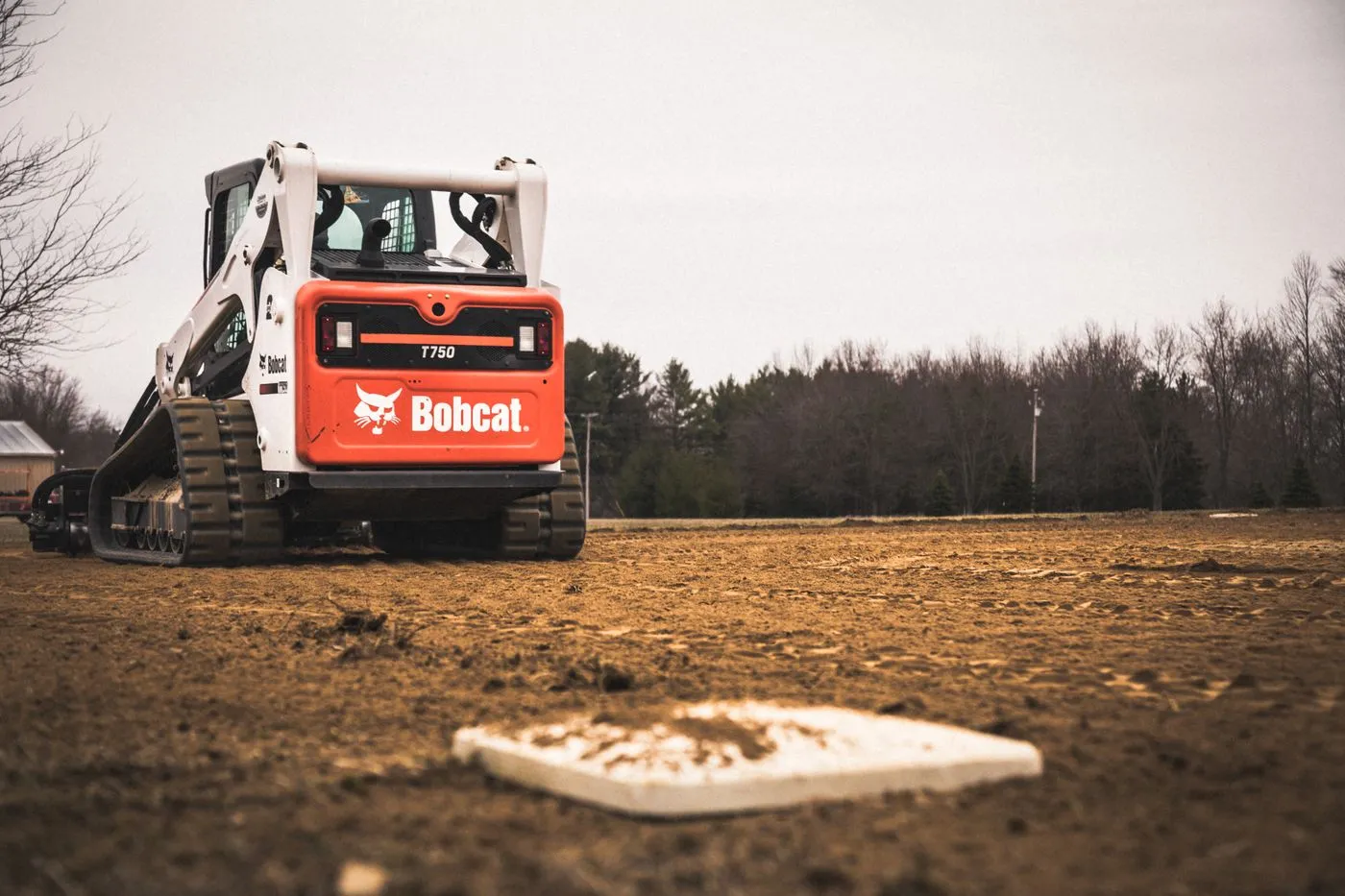 Compact track loader working a cleared dirt lot in front of a tree line